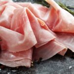 Sliced ham on wooden background. Fresh prosciutto. Pork ham sliced with rosemary